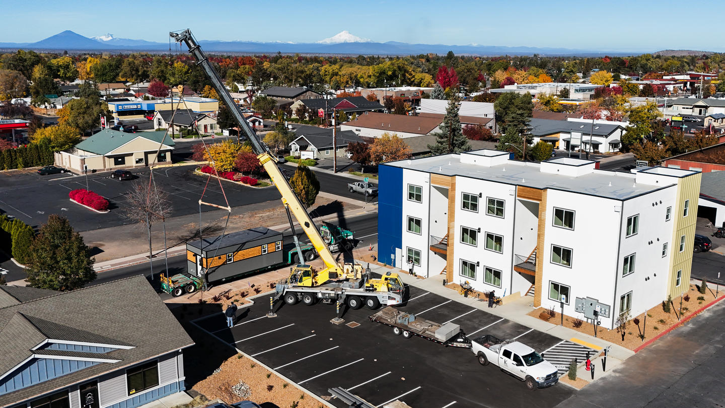 Crane setting a Timbergon modular ADU unit onto its foundation beside a completed building