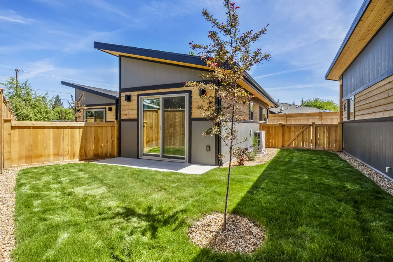 Rear exterior of a Timbergon modular ADU in Central Oregon with slider patio door, mini-split condenser, and landscaped fenced yard